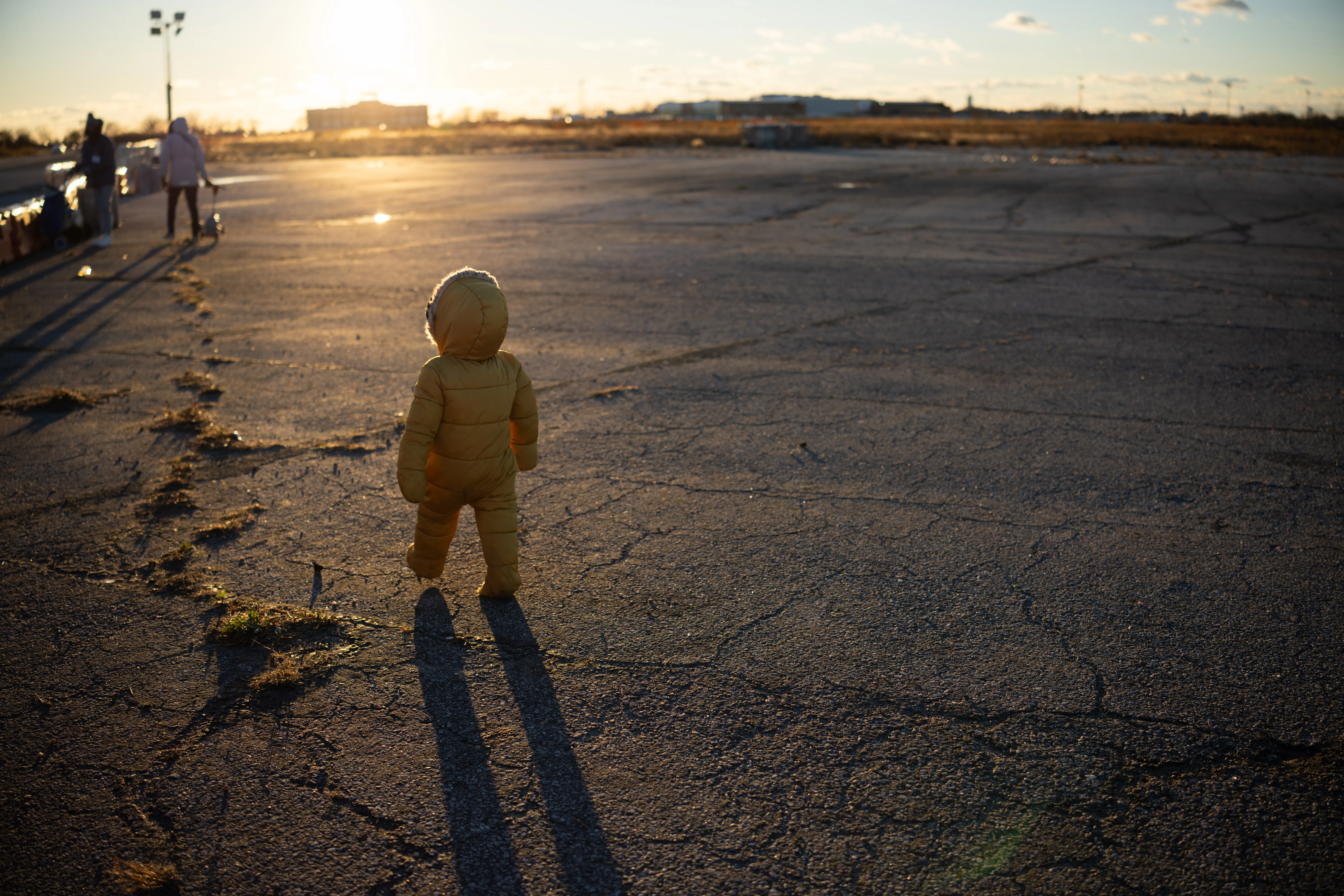 Child walking in an empty parking lot, wearing a puffy yellow coat